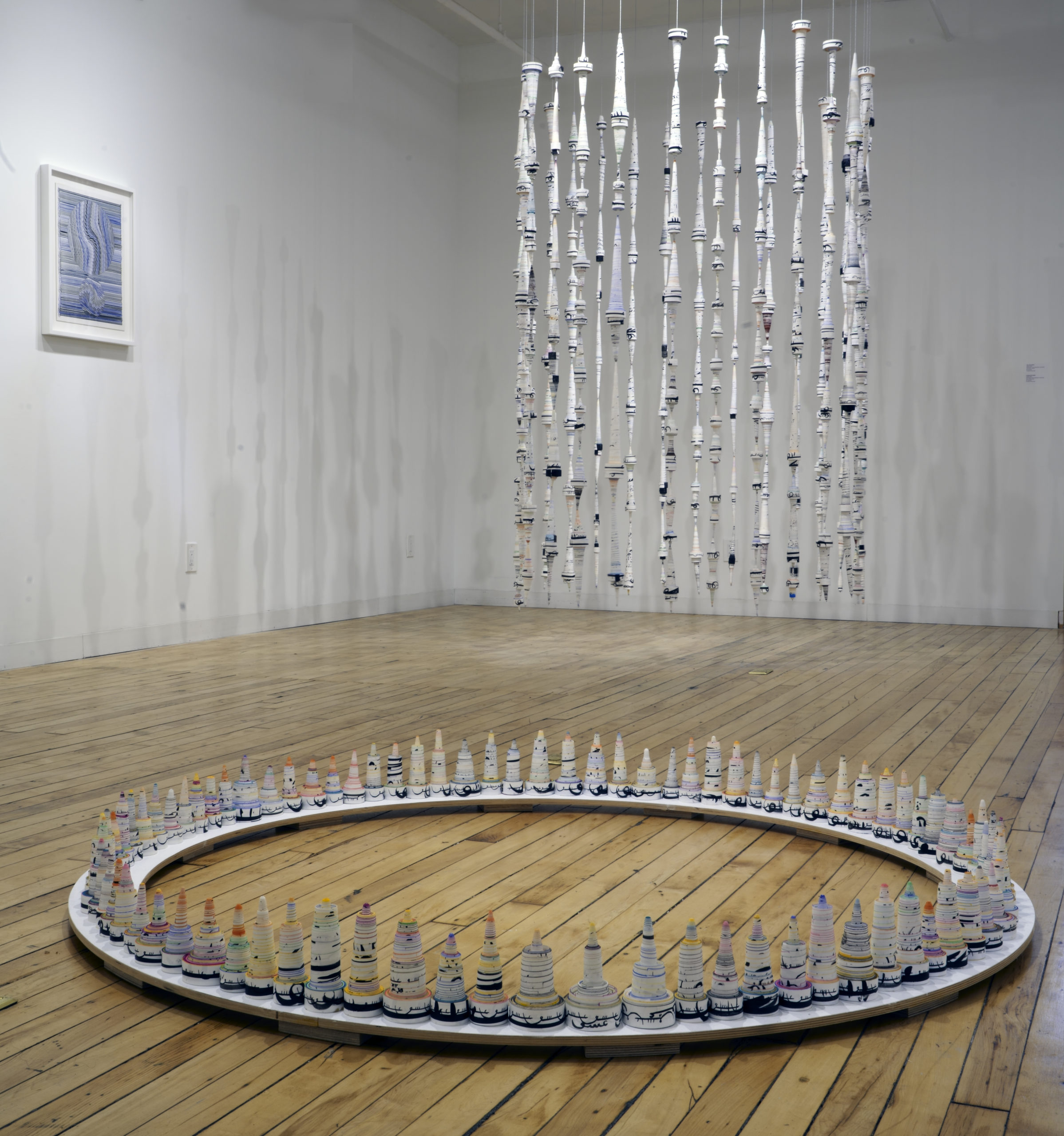 Installation view of circular artwork on the floor and hanging artwork made of paper scrolls. By Hadieh Safie 2020.