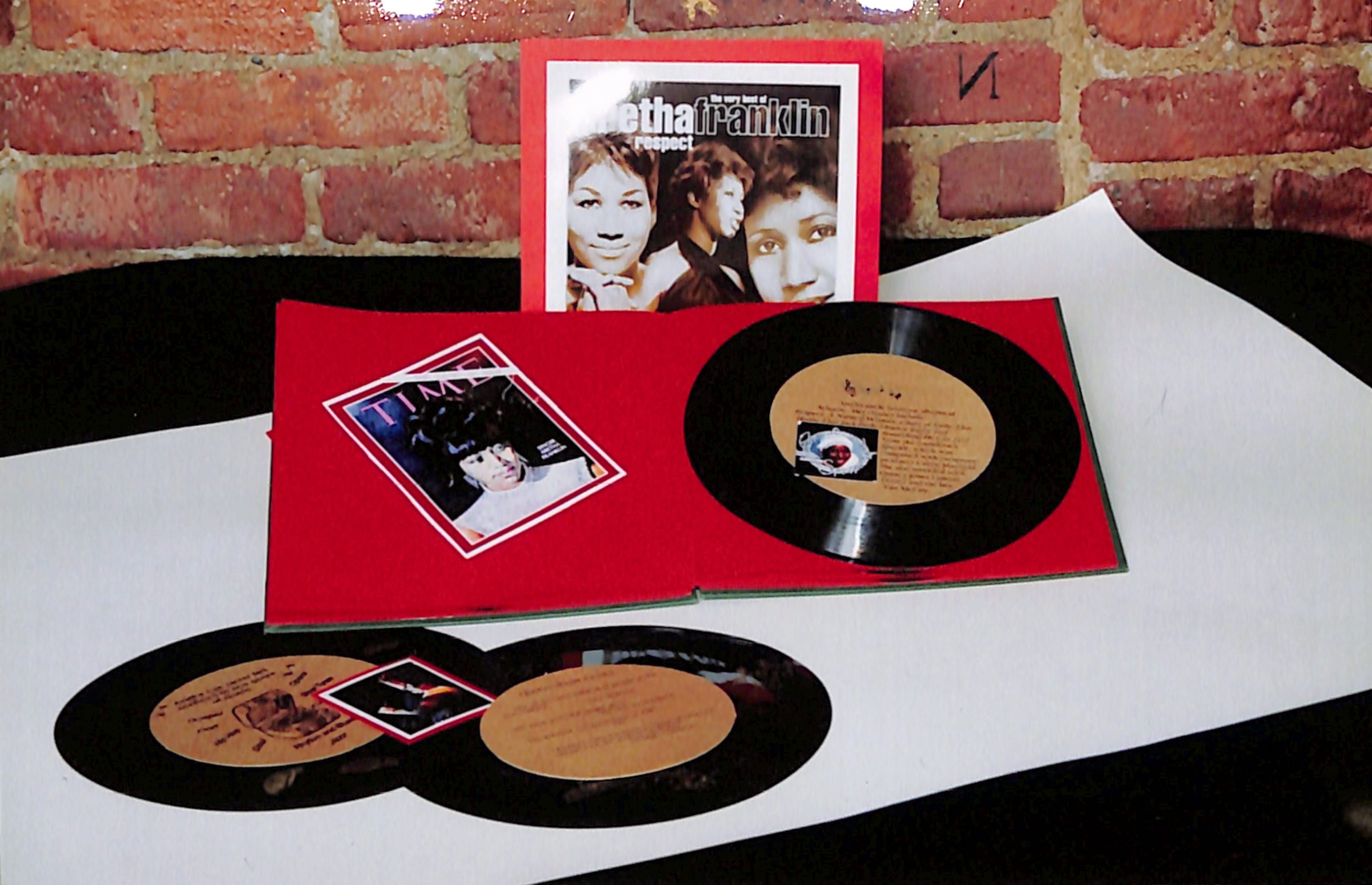three vinyl records on a table with a book about Aretha Franklin