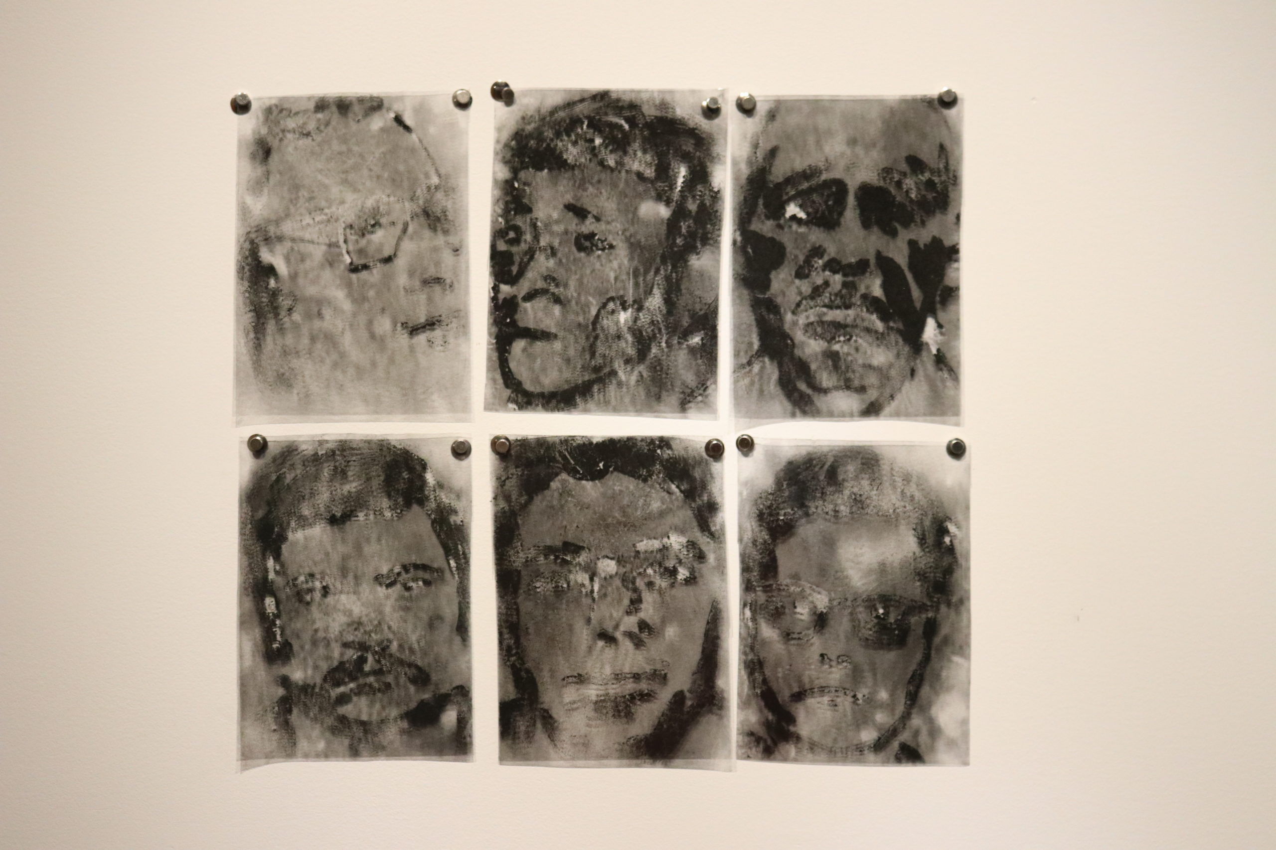 six charcoal paintings of faces on plastic