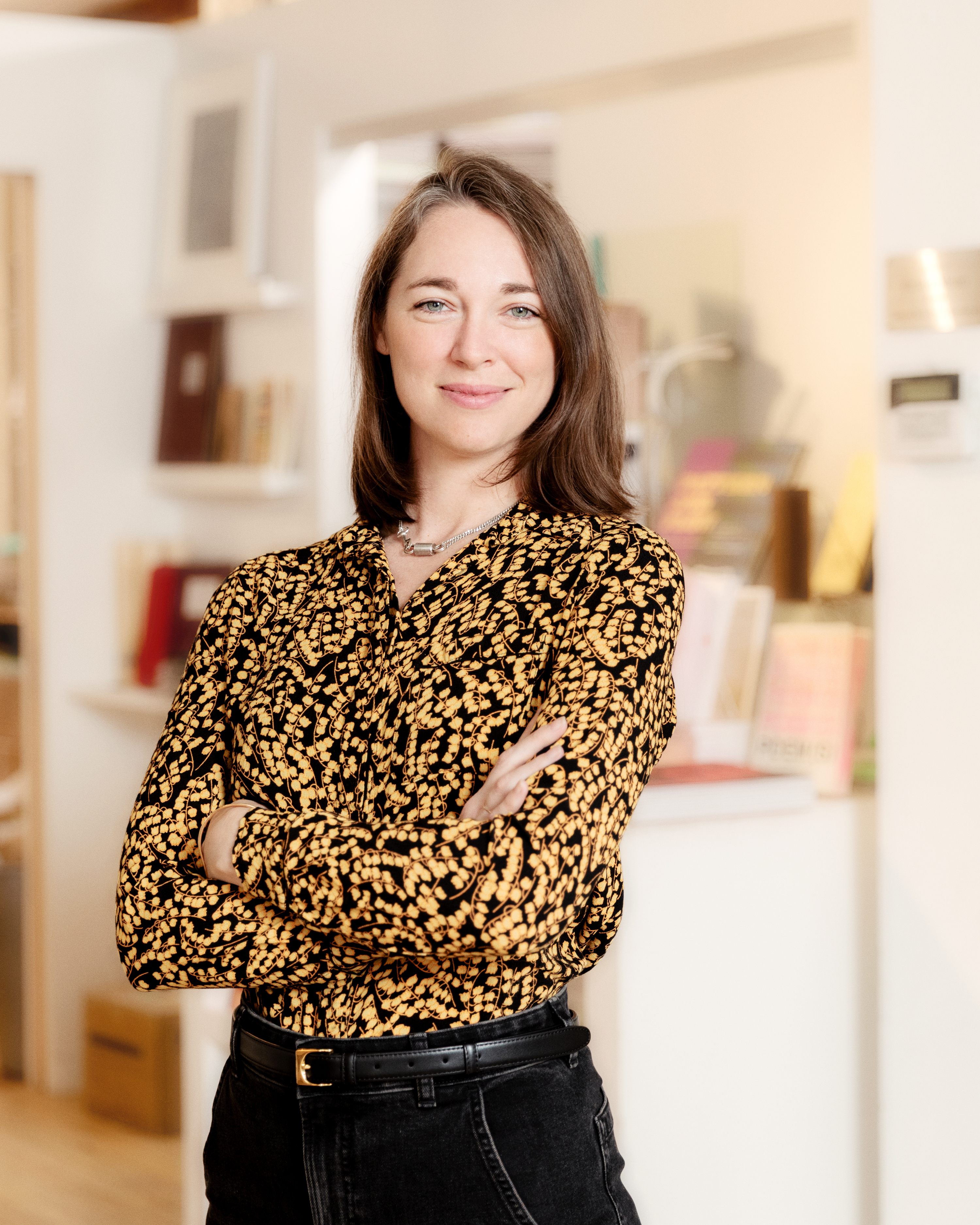 Woman with shoulder length hair stands smiling in a bookshop