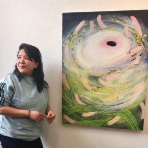 Tammy Nguyen with long black hair stands next to one of her paintings