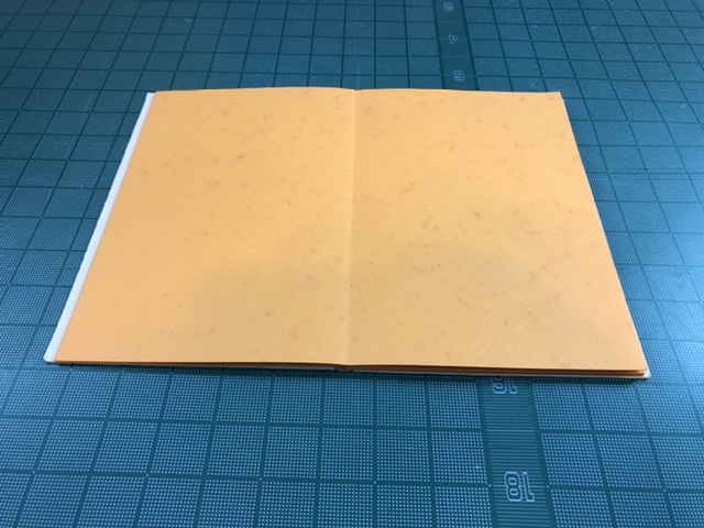 A beige soft cover drum leaf book is open flat on a cutting board.