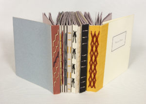 Colorful spines of 1, 2, & 3 section books are lined next to each other. The spines are a range of colors and the thread seen along them is decorative.