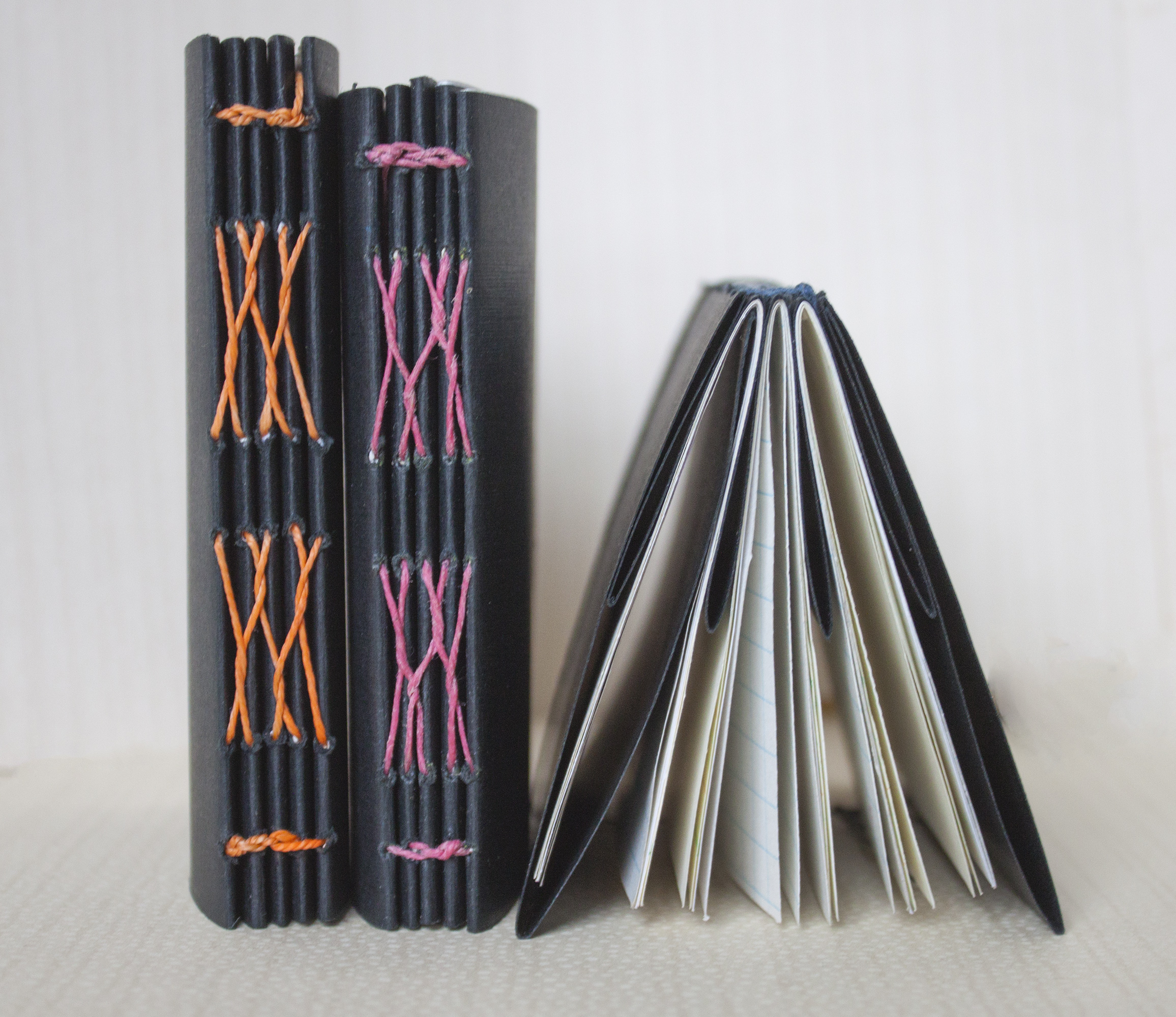 three french-link bound books are standing next to one another. One is face down while the other two are side by side.