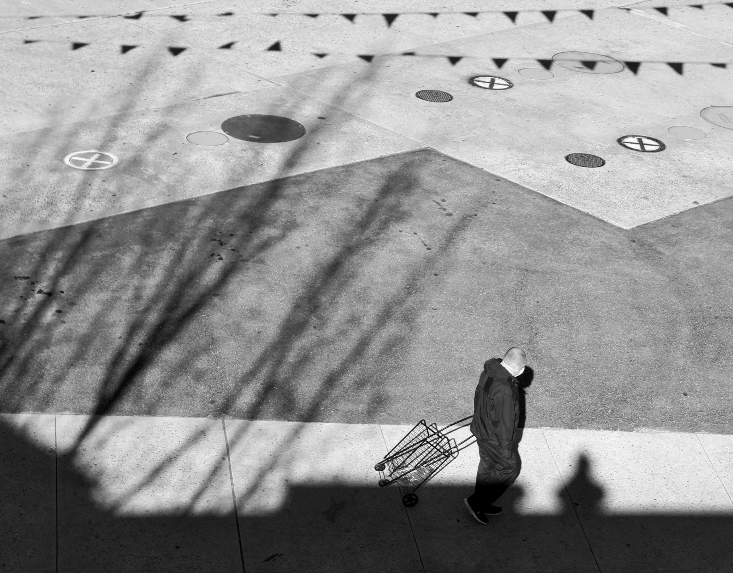 Black and White photograph taken from the rooftop, of a man walking among shadows spread across the ground