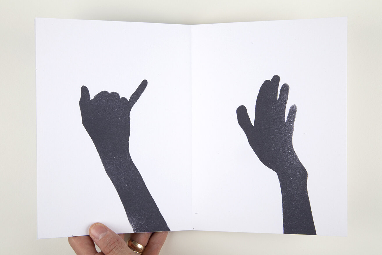 Open white book over white background. On the left page there is a black hand trying to reach another hand on on the right page.