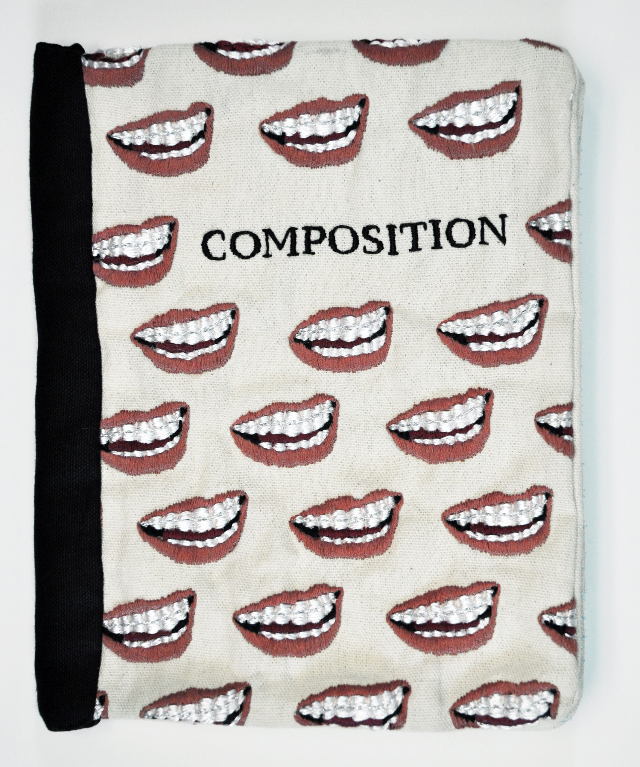 Embroidered composition notebook by Candace Hicks. There are open grimacing mouths embroidered across the cover.