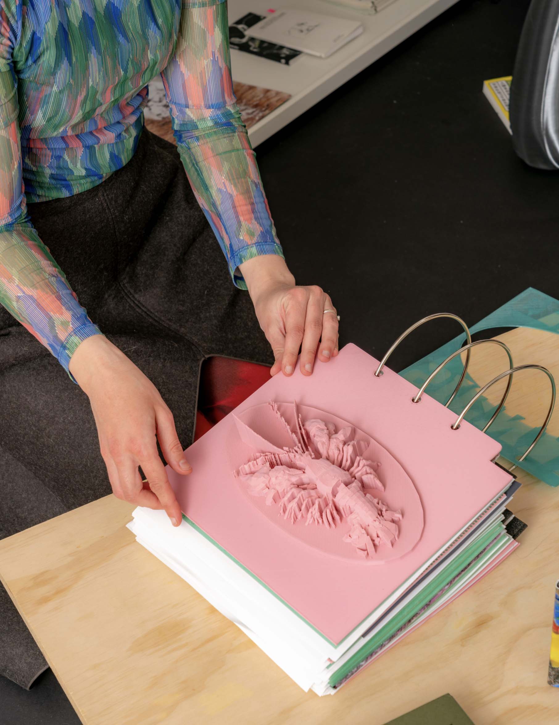 Photo of a person holding a 3D printed book page that is depicting a crawfish. The page is pink.