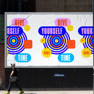 A photograph of a person walking in front of a graphic billboard that repeats the phrase "Give Yourself Some Time" in bold, bright colors.