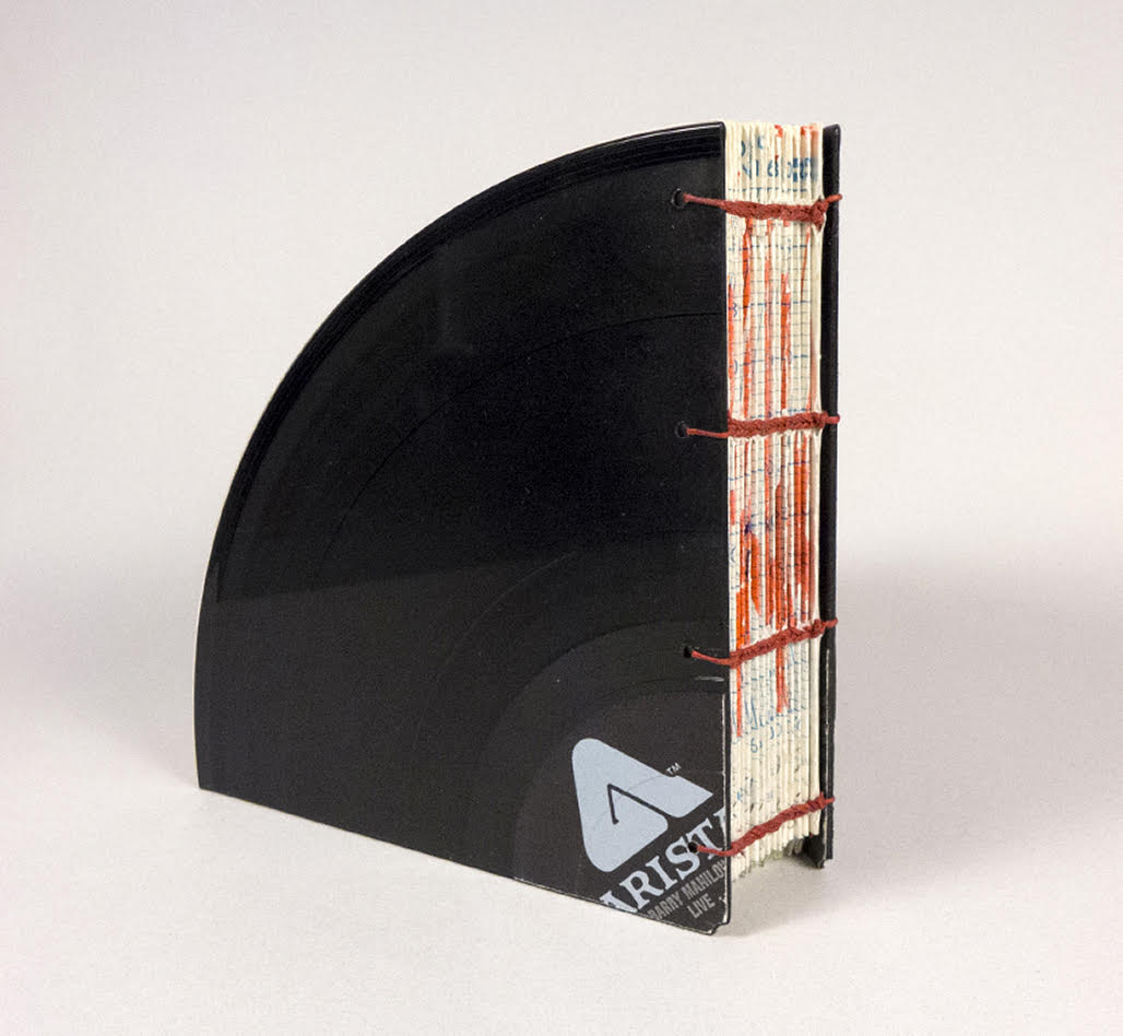 Image of a book cover made of one-fourth of a vinyl record, with an open spine stitched with red thread.