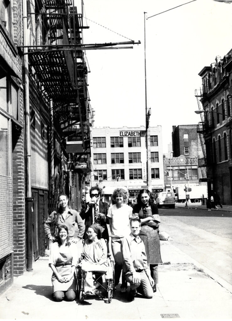 Black and white photograph of Outside of Center for Book Arts original location at 15 Bleecker Street, New York City. 
(Clockwise from top left: Unknown, Richard Minsky, Kathy Weldon, Barbara Mauriello, Dikko Faust, a woman in a wheelchair named Cindy (at one point CBA's bookkeeper, surname currently unknown), Mindy Dubansky, and an unknown woman outside CBA's original location 