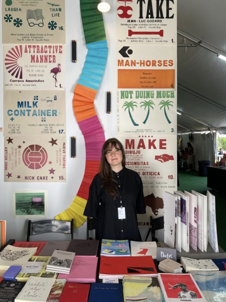 woman stands behind book fair table with colorful books
