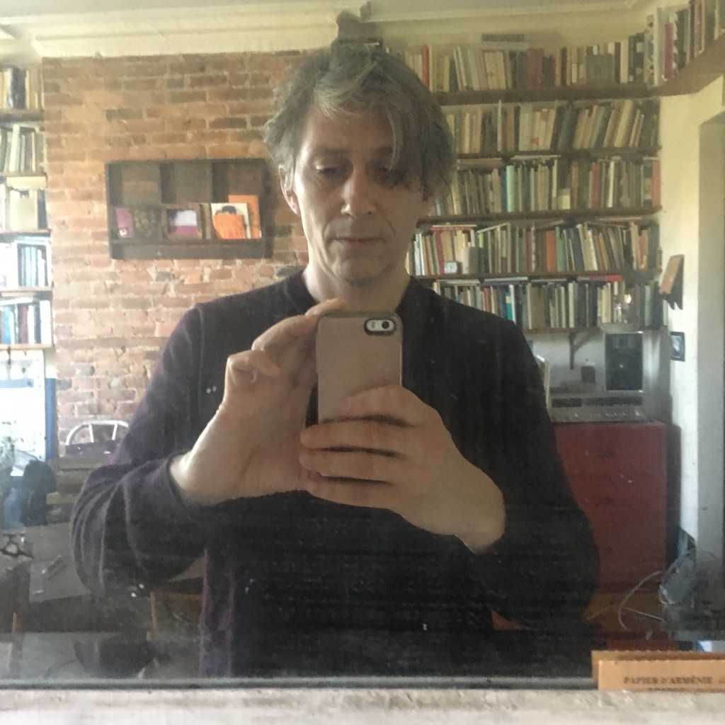 man with messy gray hair photographs himself in a mirror with an iphone