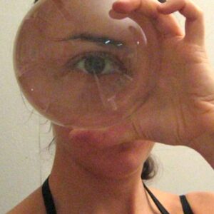 Alta hold a glass sphere in front of their eye, magnifying their eye so it takes up their whole face.