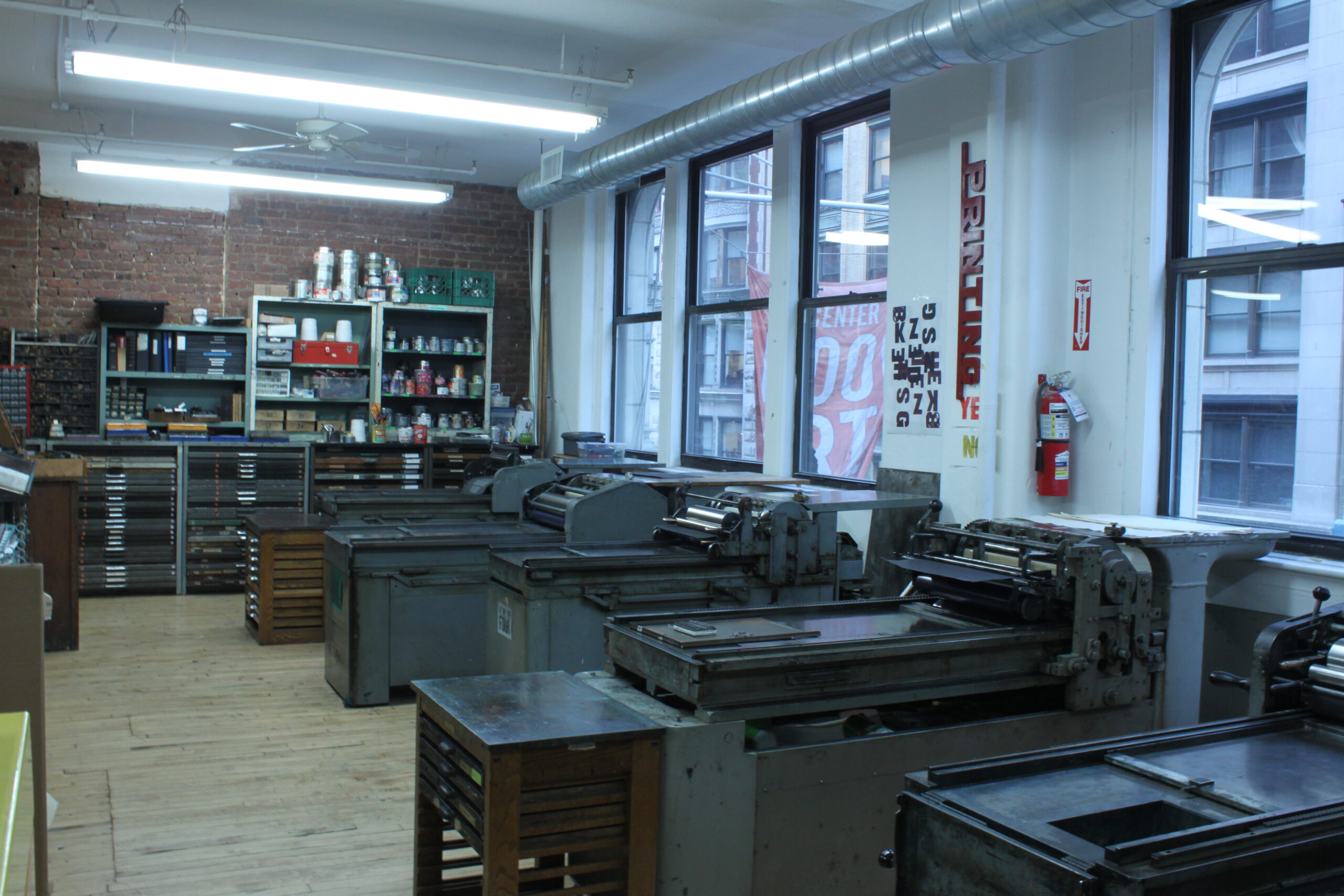 A view of the letterpress studio at CBA. A long row of windows on the left, in front of which are five Vandercook presses.