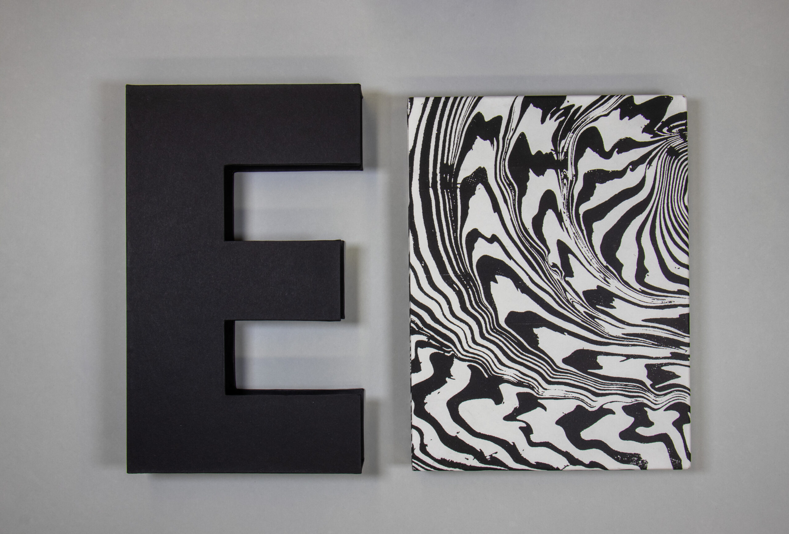 Two interlocking slipcases, on cut into the shape of an E and the other marbled in black and white.